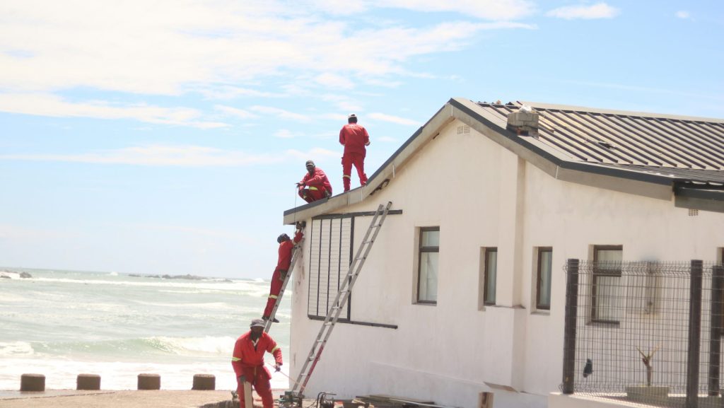 Workers in red suits on a white building roof